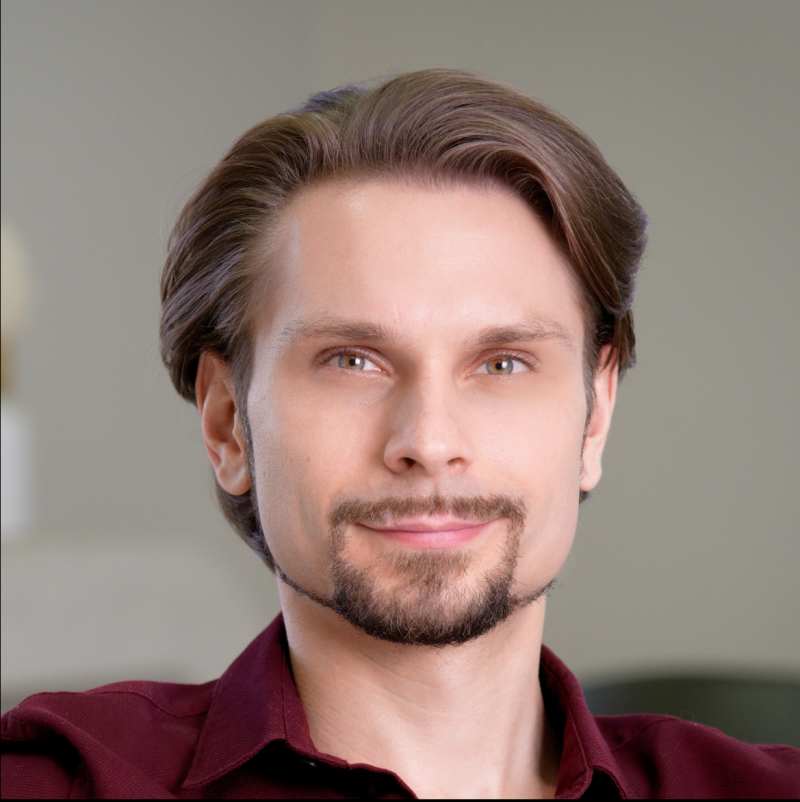 A portrait of a man with brown hair, hazel eyes, and a dark goatee, wearing a maroon button-down shirt.