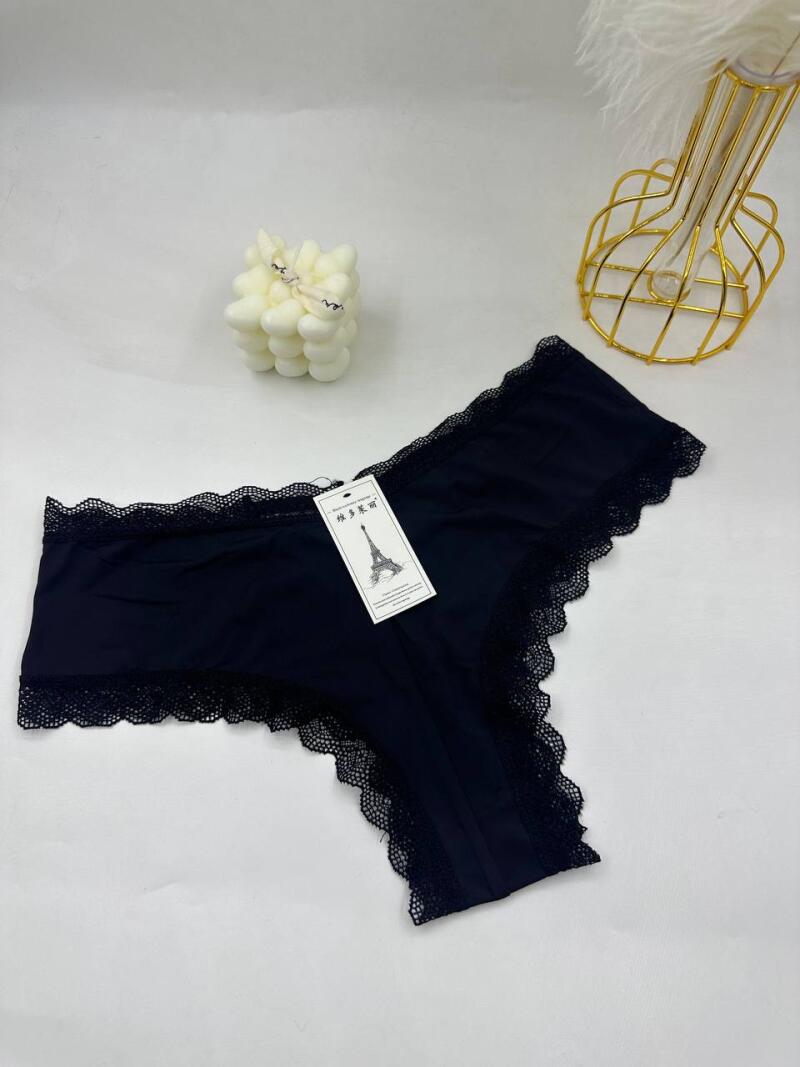 Black lace-trimmed underwear sits on a white surface with a tag that has an image of the Eiffel Tower, along with a white bubble candle and a gold metal vase in the background.