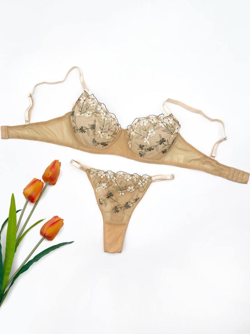 A beige lingerie set with floral embroidery is arranged with three orange tulips on a white background.