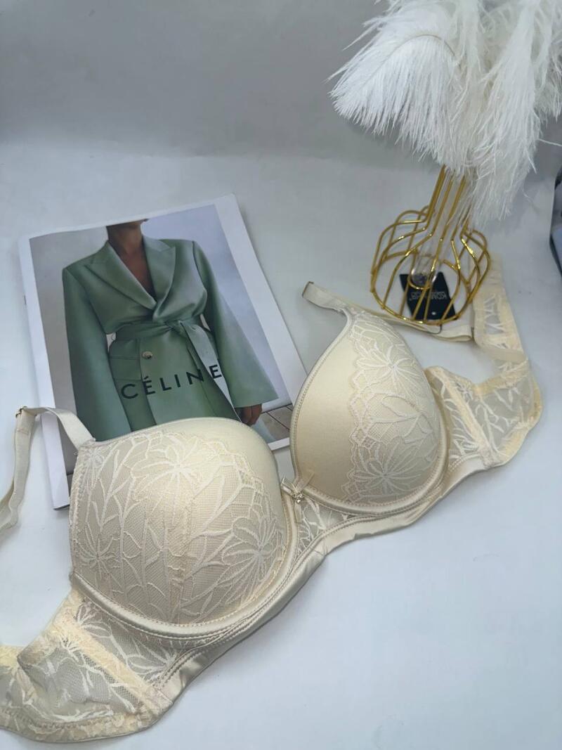 A cream-colored bra with lace detailing sits next to a fashion magazine with the word "CÉLINE" visible on the cover, alongside a decorative golden stand holding white feathers.