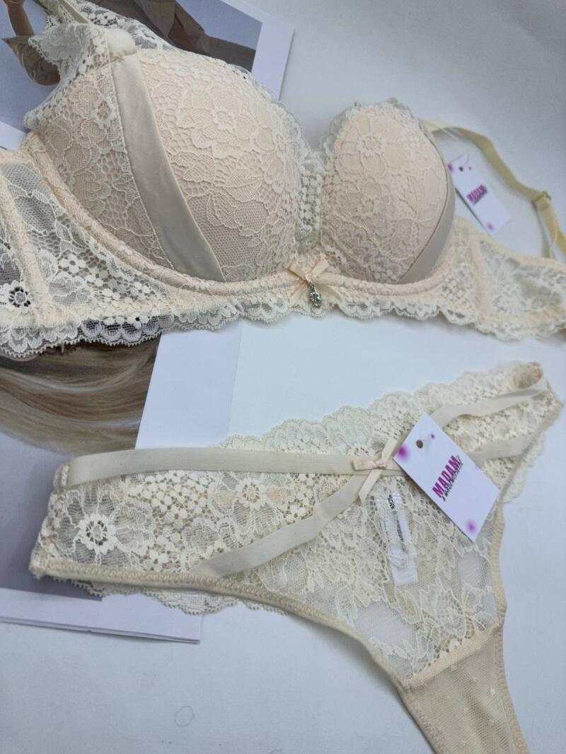 A beige lace bra and matching thong are displayed with tags attached, positioned on a white surface with a magazine underneath.
