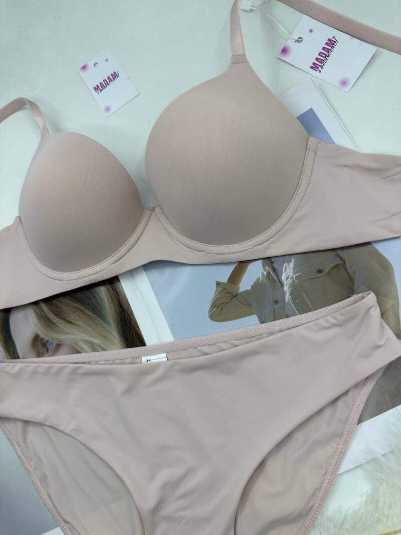 A beige bra and panty set is displayed against a backdrop of a magazine page featuring a woman, with tags reading "MADAM" visible.