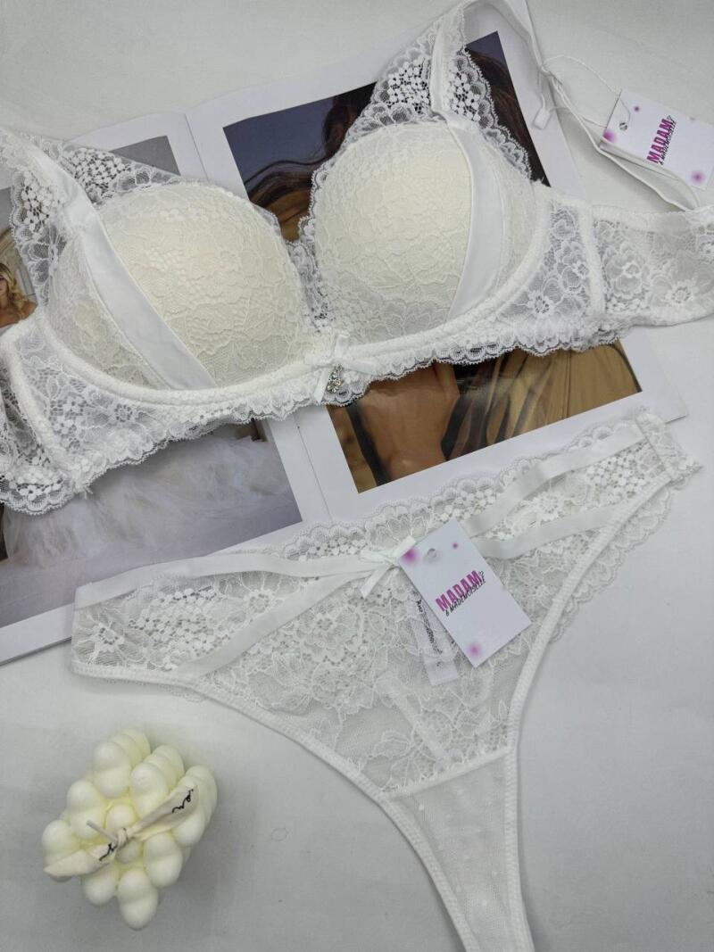 A white lace bra and panties set are displayed on a magazine, with the "MADAM" brand tag visible on both items.