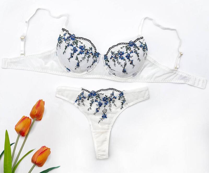 A white lingerie set with blue floral embroidery is displayed with three orange tulips on a white background.