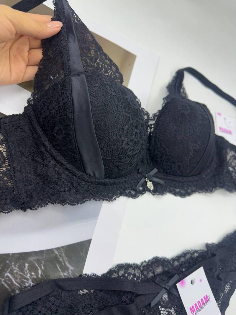 A black lace bra and panty set is displayed, with a hand holding the bra and a tag with the word "MADAM" visible on the panties.