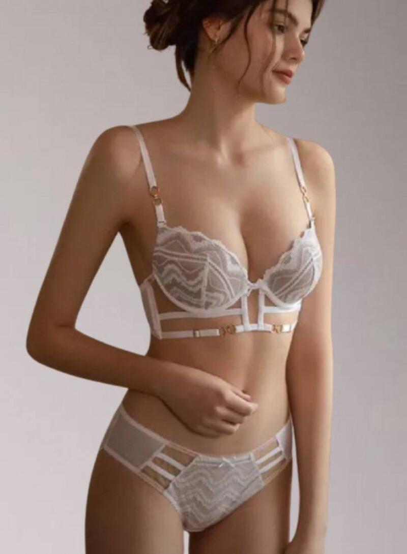 A woman poses in a matching white lace bra and panty set with strap details.