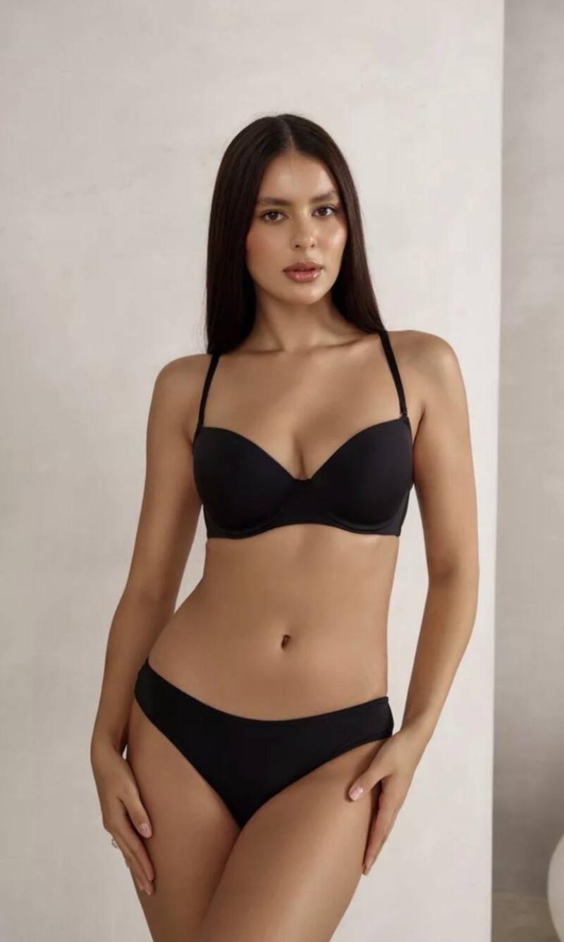 A woman with long dark hair is posing in a black bra and panties.