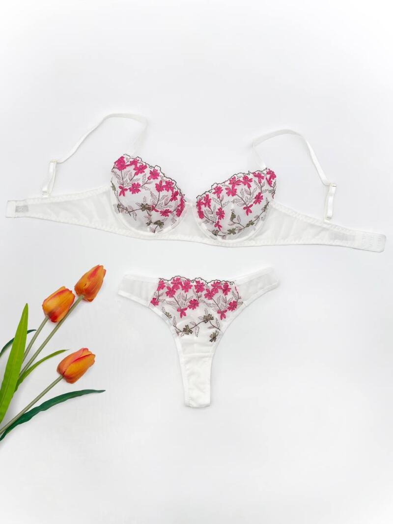 A set of white lingerie with a floral pattern is displayed next to three orange tulips with green stems on a white background.