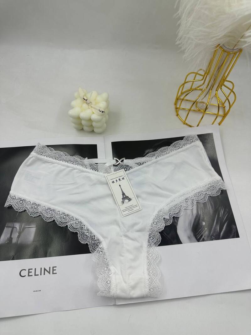 The image shows white lace-trimmed panties with a tag featuring an image of the Eiffel Tower, placed on a magazine with the text "CELINE". There is also a decorative candle and a feather holder in the background.