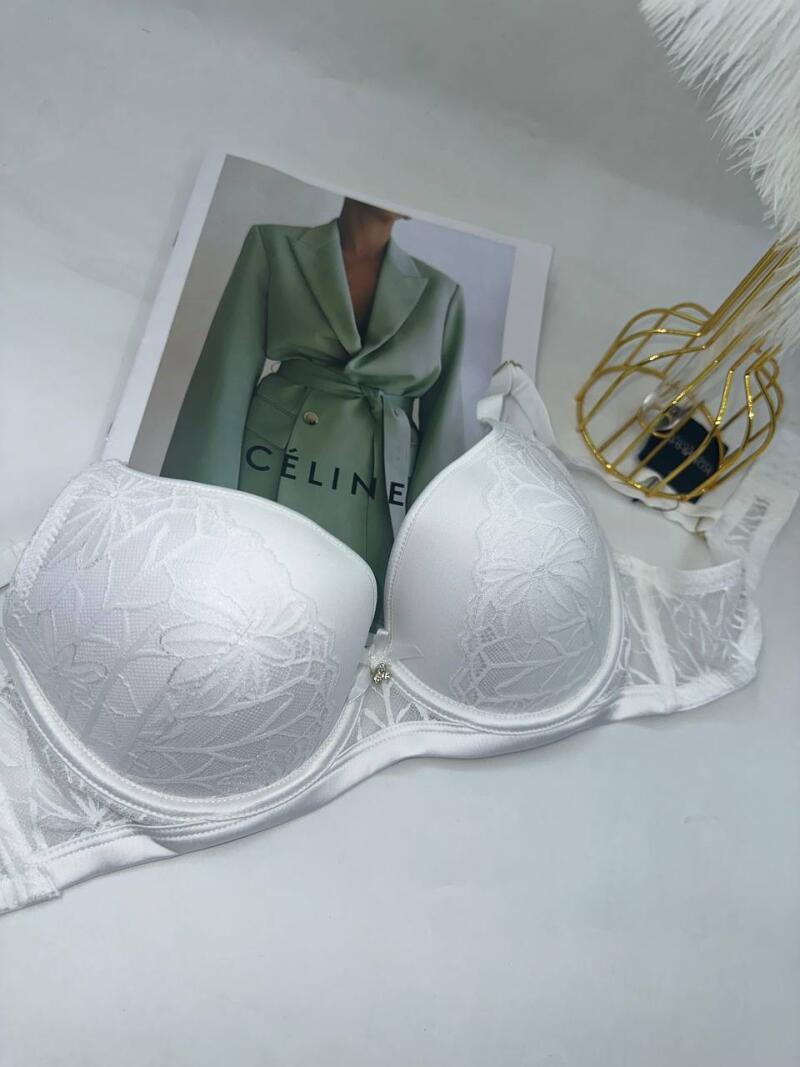 A white lace bra is placed on a white surface, next to a magazine with the text "CÉLINE" and a golden decorative object.