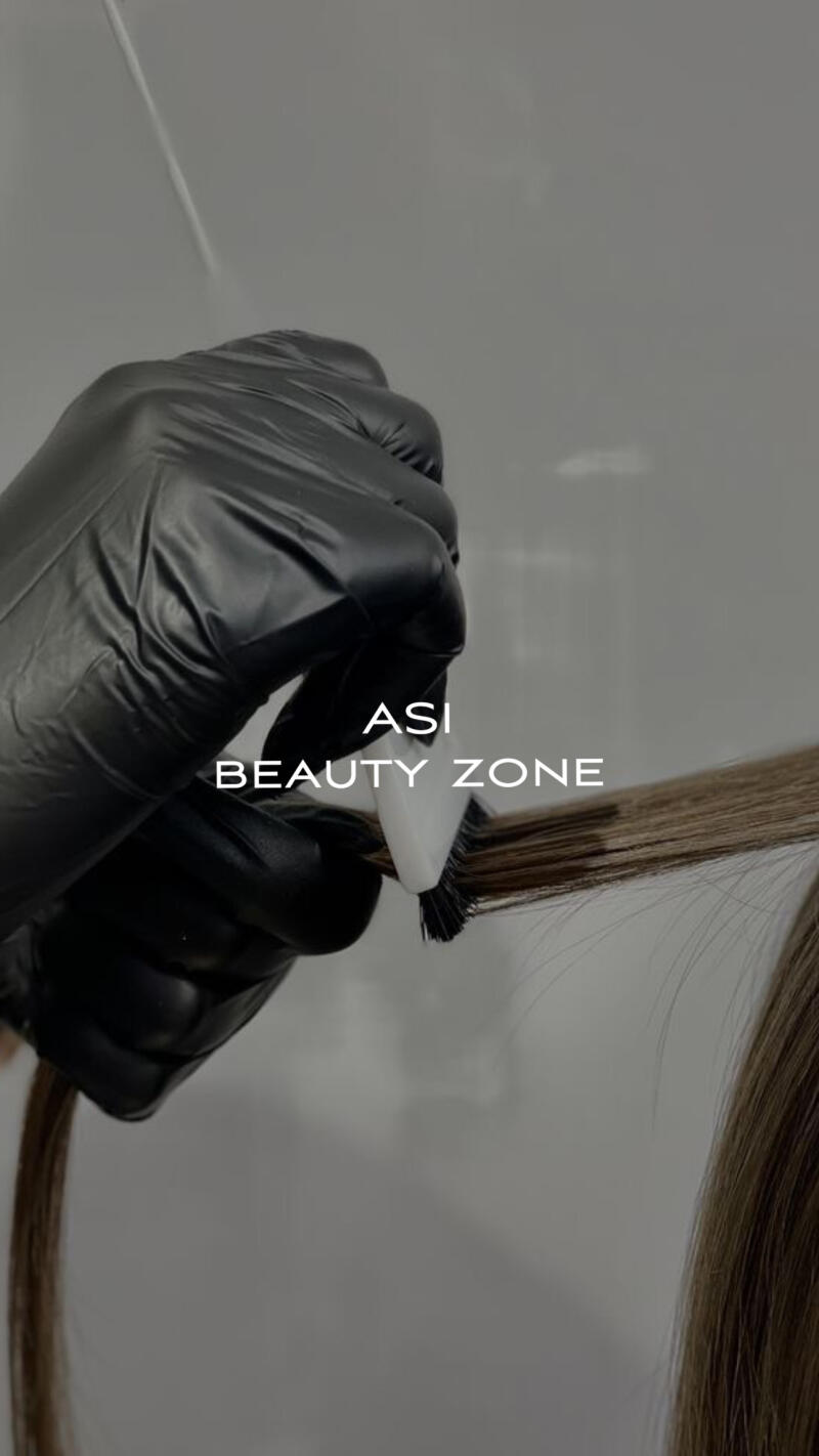 A hand in a black glove applies hair dye to brown hair with a brush; the text "ASI BEAUTY ZONE" is superimposed.