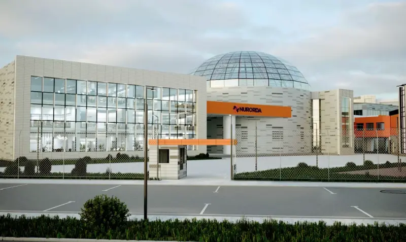 The image shows the exterior of a modern building complex with the name "NURORDA" prominently displayed in orange lettering above the entrance. The complex features a domed glass structure and surrounding office buildings with large windows.