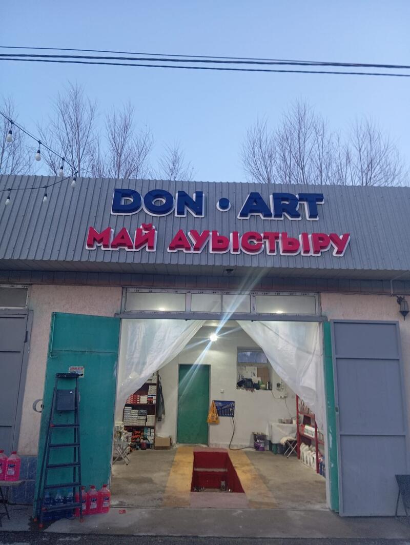 The photo shows the facade of a building with the sign "DON ART MAЙ АУЫСТЫРУ", which appears to be a car service station with an open garage door revealing a service pit.