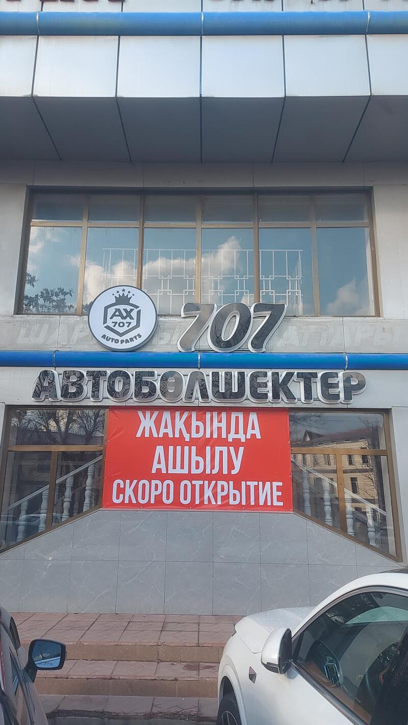 The building features signs for "AX 707 AUTO PARTS" and "707 АВТОБОЛШЕКТЕР," along with a red banner announcing "ЖАҚЫНДА АШЫЛУ / СКОРО ОТКРЫТИЕ" (opening soon in Kazakh and Russian).