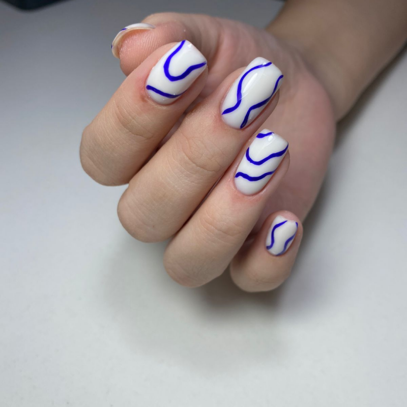A hand displays a manicure with white nails and a blue wavy line design.