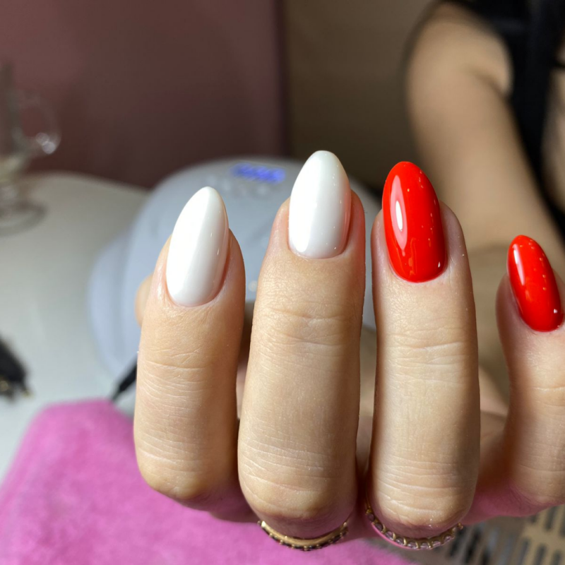 A close-up shows a hand with almond-shaped nails, two painted white and two painted red.