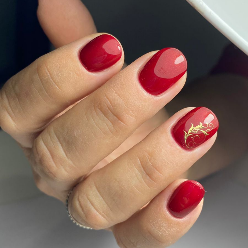 A hand with red polished nails, one with a gold floral design.