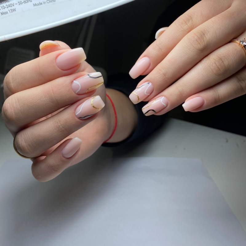 The image shows manicured hands with light pink, square-shaped nails adorned with gold and black line art.