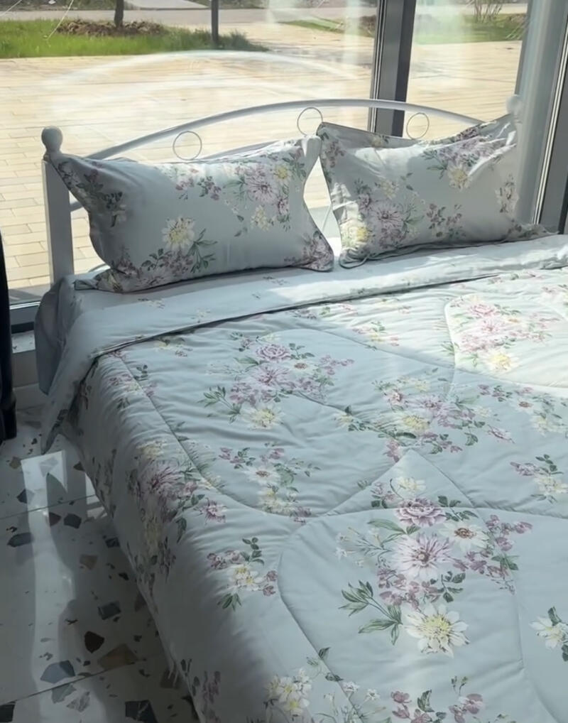 A made bed with light blue floral bedding and pillows is positioned near a window.