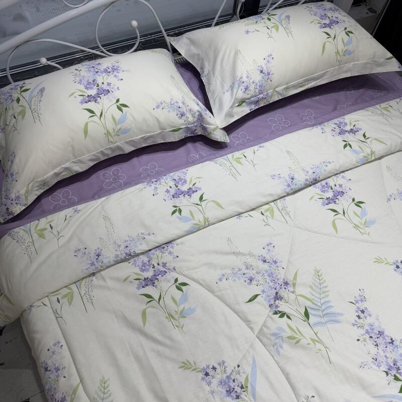 The bed has white sheets and pillowcases decorated with purple flowers and green leaves, and a purple trim.