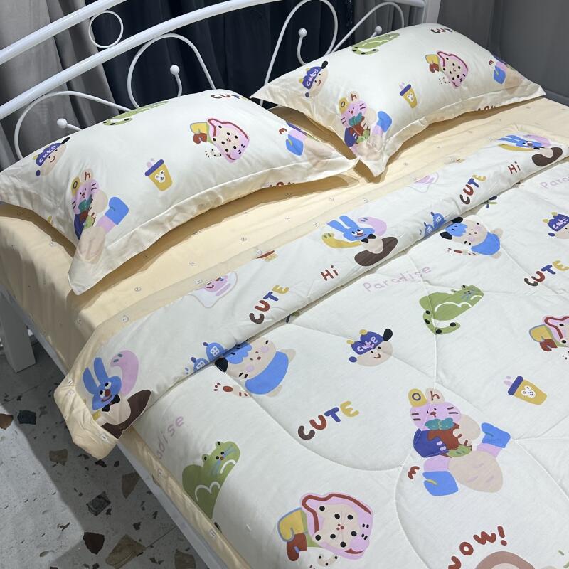 A bed with a white metal frame is covered with a light yellow sheet and a comforter and two pillows patterned with cartoon figures and the word "CUTE."