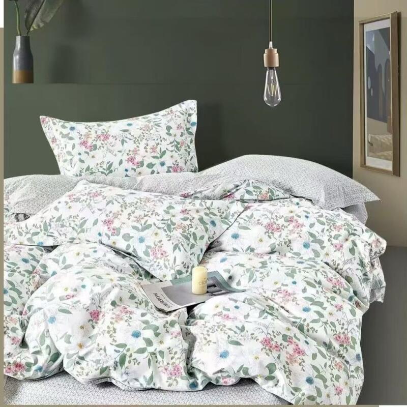 A bed is covered in white floral patterned bedding, featuring pink and blue flowers with green leaves, with a magazine and candle placed on top, set against a dark green wall with a hanging light bulb and framed picture.