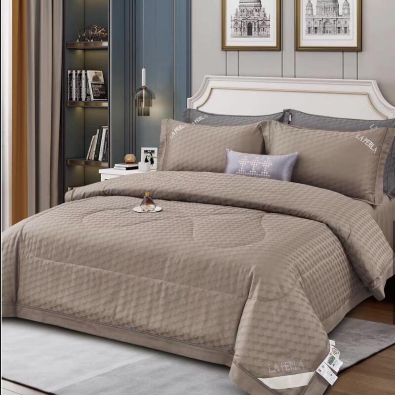 A neatly made bed with brown bedding, including pillows and a duvet, is centered in a room featuring a bookshelf, artwork, and curtains; "LA PERLA" is printed on the bedding.