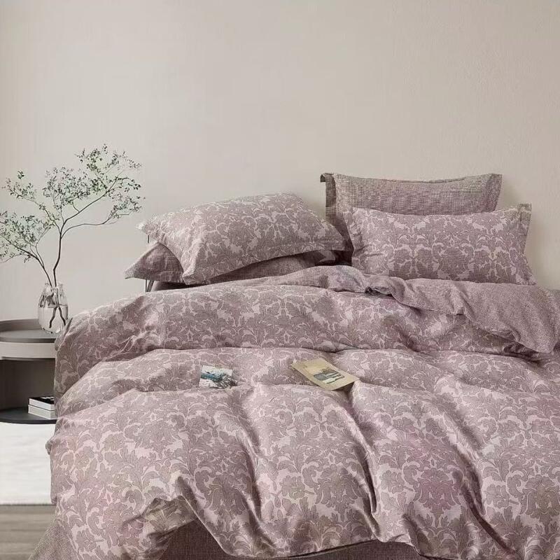 A bed is made with patterned bedding and pillows, with a small table next to it holding a vase with branches.