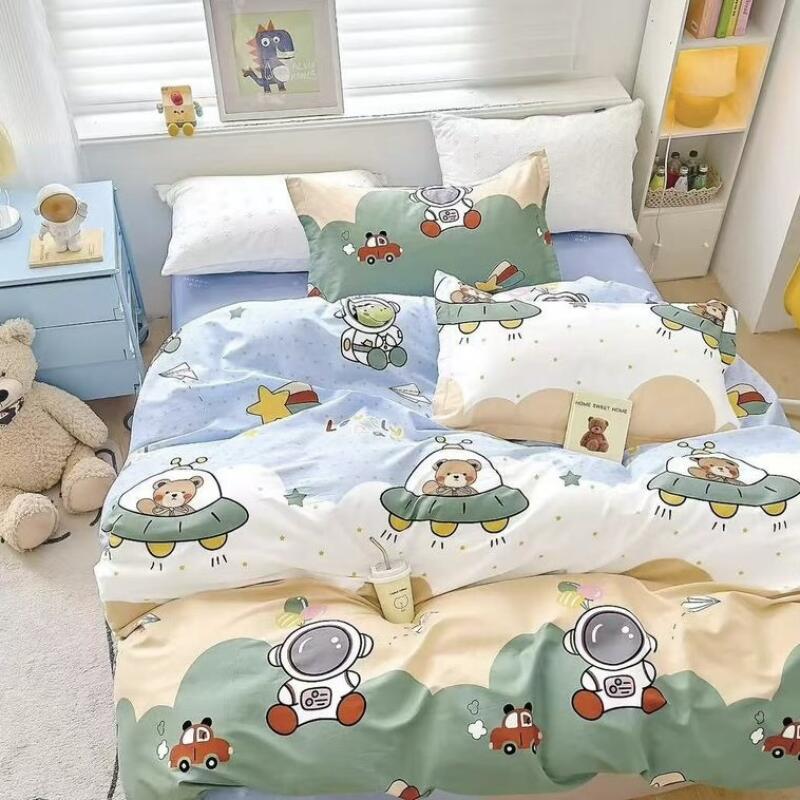 A bed is covered with a colorful, cartoon-themed comforter featuring astronauts, cars, and bears in UFOs; a teddy bear sits on the floor next to a light blue nightstand.
