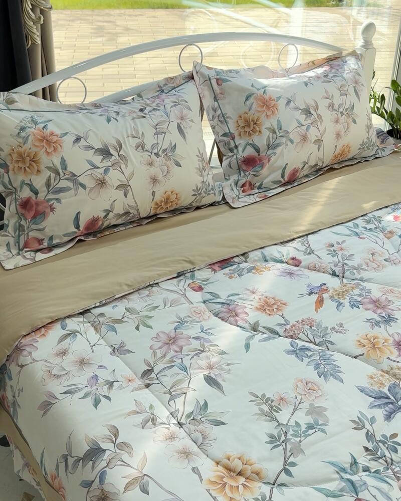 A bed with a white metal frame is neatly made with floral-patterned pillows and comforter, accented by a solid beige sheet.