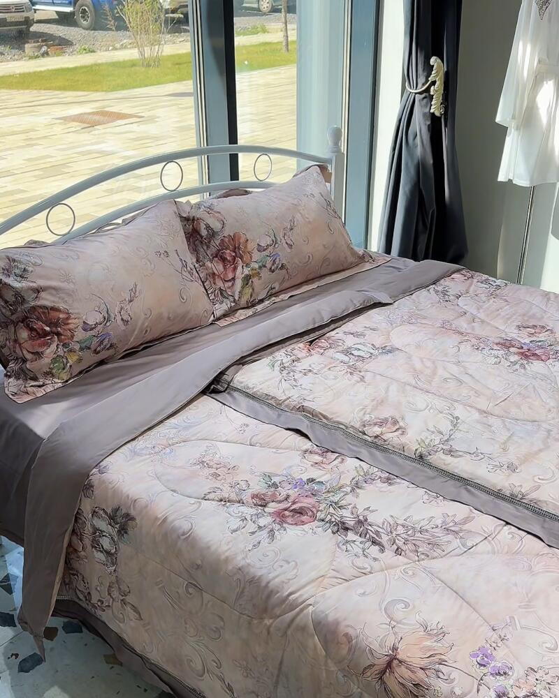 A bed is neatly made with floral-patterned bedding, including two pillows, a flat sheet, and a comforter, all in light, muted colors.