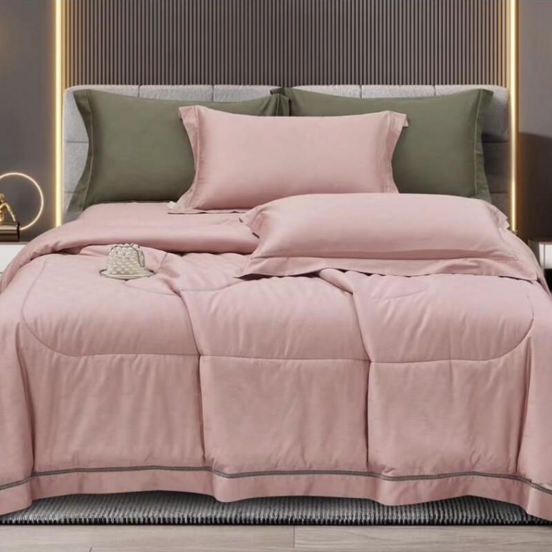 A bed is neatly made with a pink duvet, pink pillows, and two olive green pillows, set against a gray headboard with vertical lines.