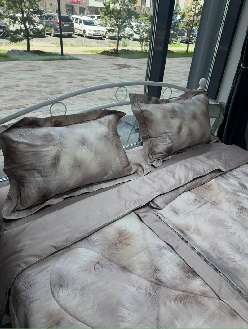 A bed with patterned bedding, including pillows and a comforter, is positioned in front of a large window.