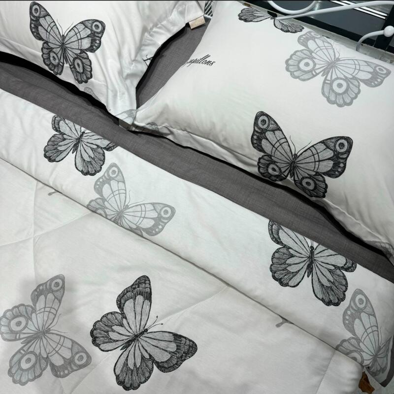 A close-up of bedding with a white base and gray butterfly patterns, including pillows and a comforter.