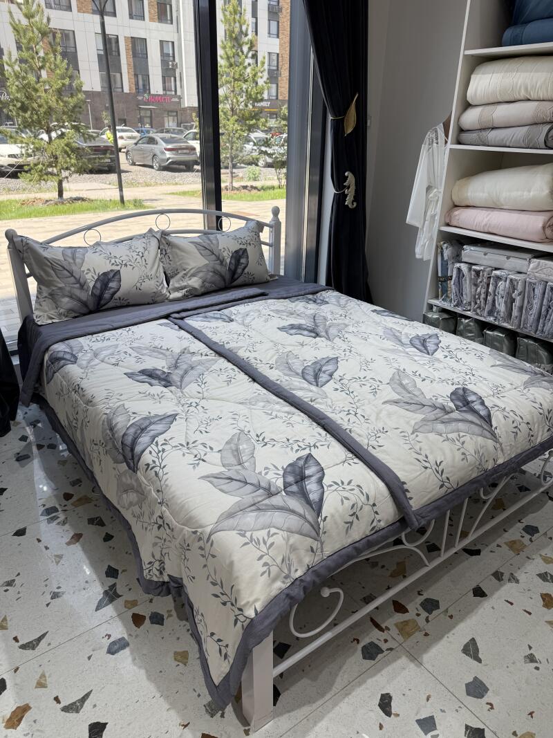 The image shows a bed with pillows and a blanket with a leaf pattern, along with a shelf unit holding folded blankets.