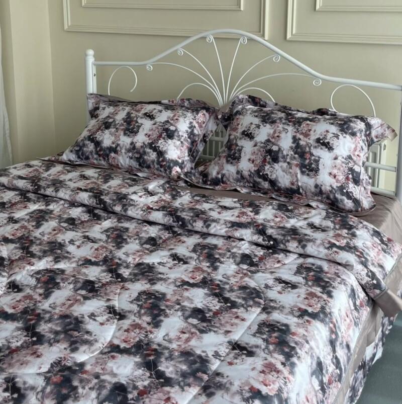 A bed with a white metal frame is covered with a floral patterned comforter and pillows.