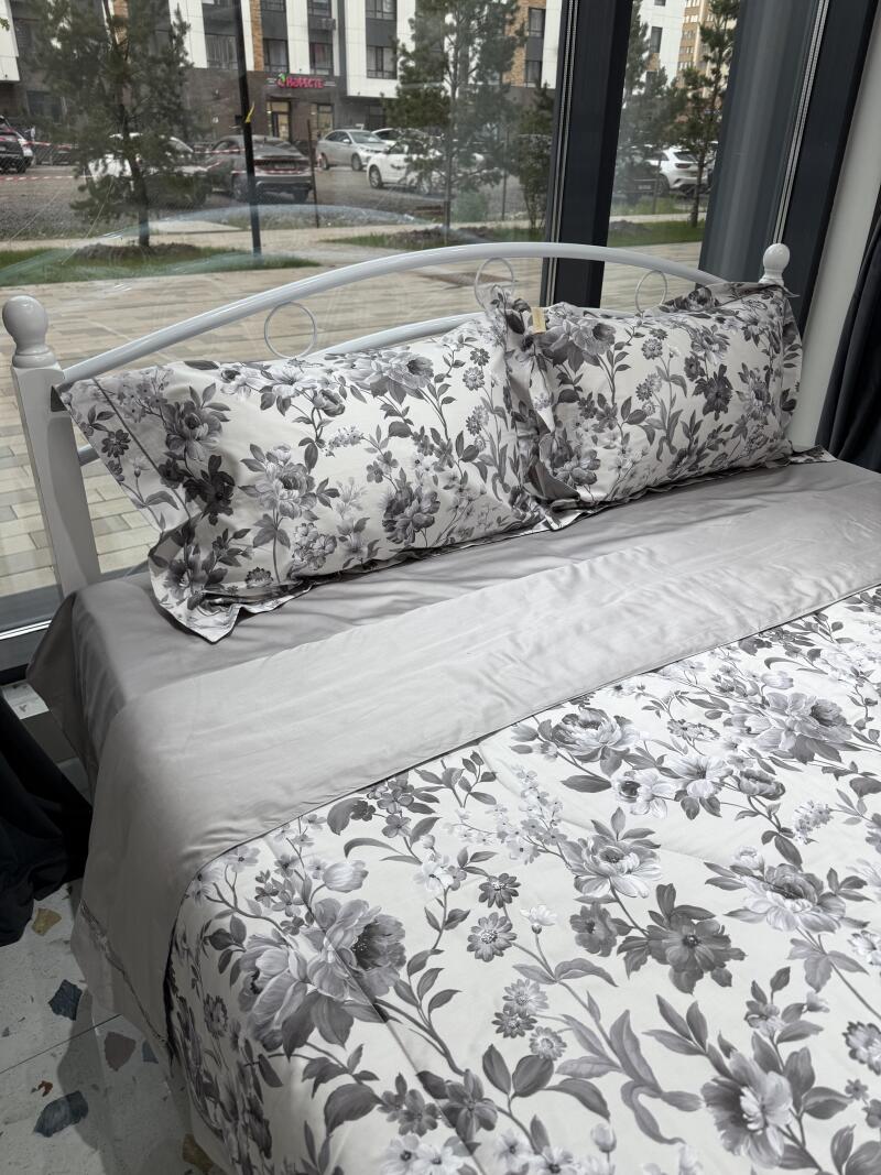 A bed with a white frame is covered in gray bedding with a floral pattern.