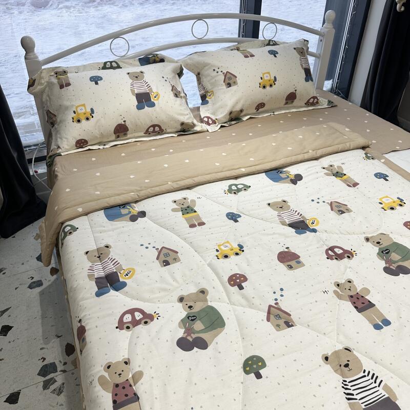 A bed with a white metal frame is covered in a beige and white patterned comforter and matching pillows featuring images of bears, cars, and houses.