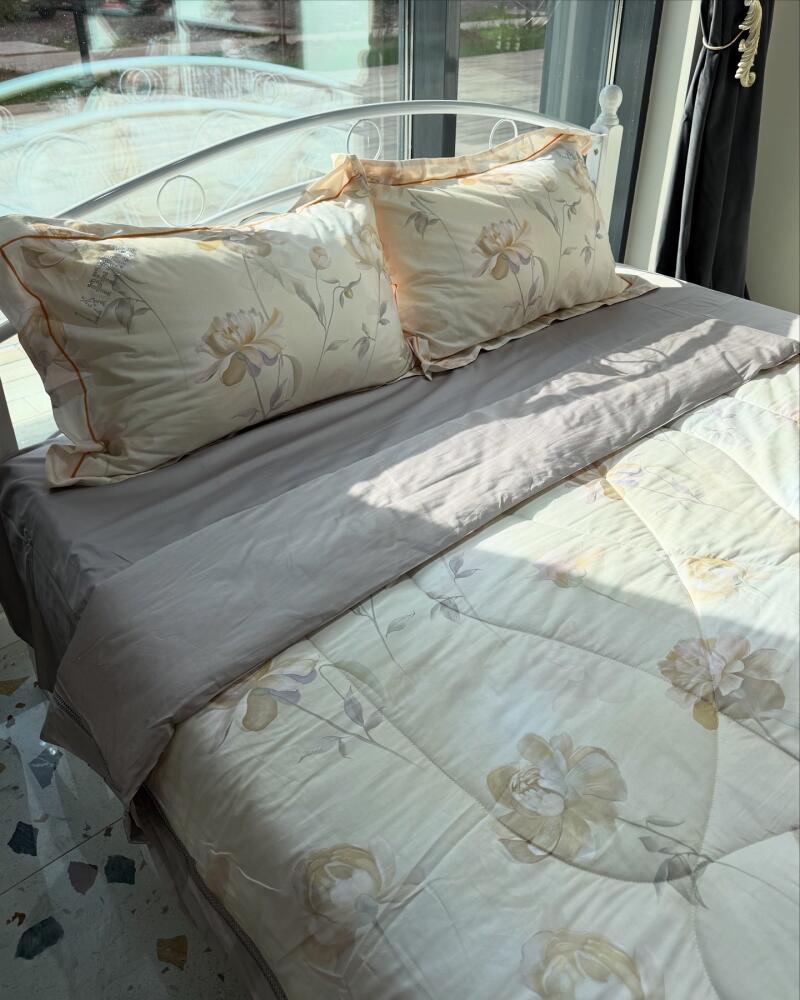A bed with floral patterned bedding, including two pillows and a comforter, is neatly made on a white metal bed frame near a window.