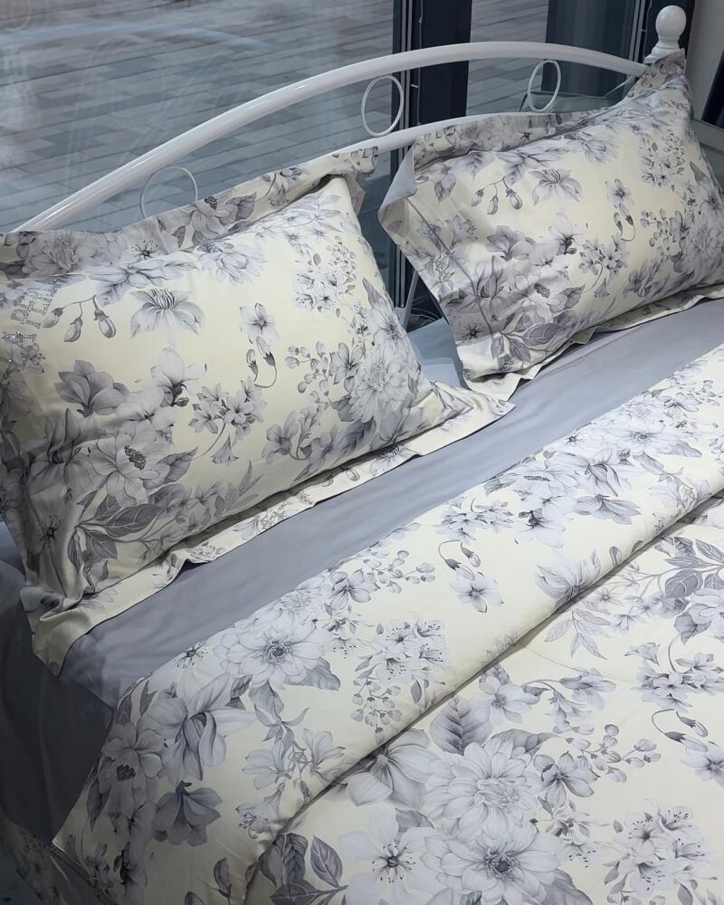 A bed with a white metal frame is covered with gray sheets and flower-patterned pillows and duvet.