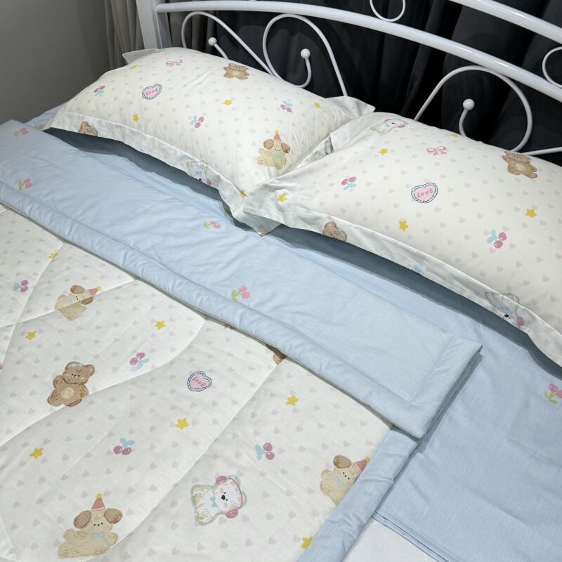 A bed with white metal frame is covered in light-colored bedding featuring teddy bear and cherry blossom patterns, complemented by a blue blanket.