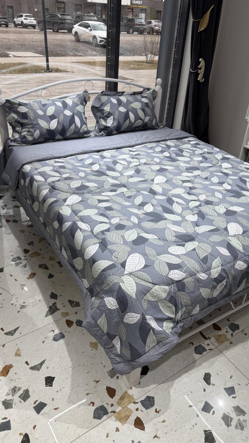 A bed is neatly made with a gray leaf-patterned comforter and matching pillows.