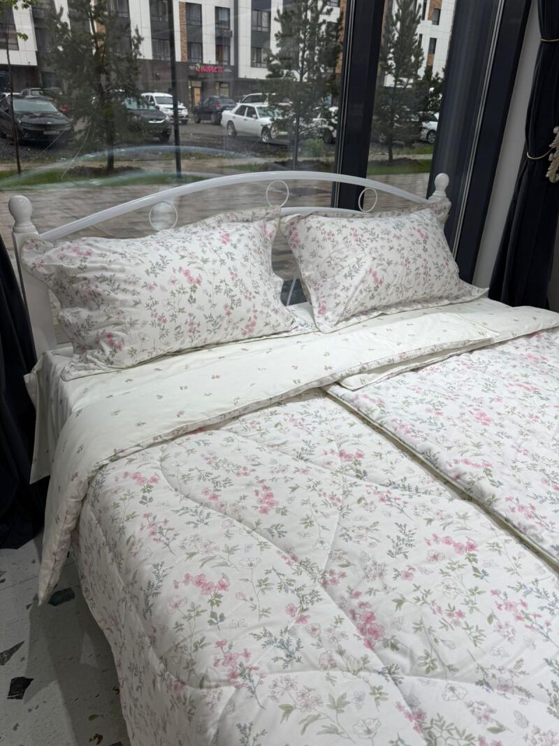 A bed with white floral bedding is positioned in front of a window, with a view of an urban landscape.