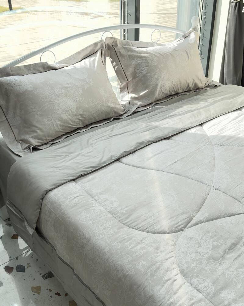 A bed is neatly made with gray bedding, including two pillows with floral designs, a comforter, and a flat sheet.
