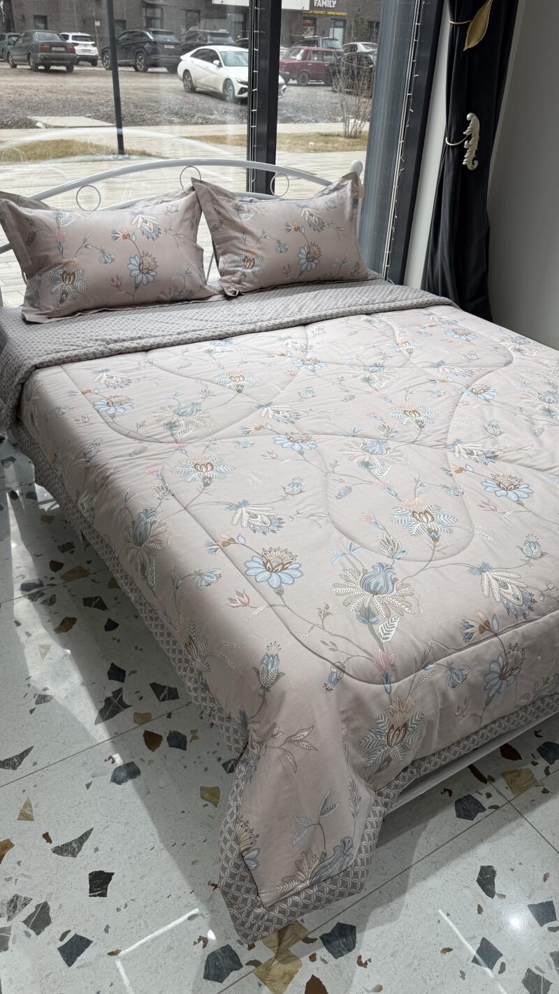 A bed is neatly made with a floral patterned duvet and matching pillows on top of a gray textured bedspread.