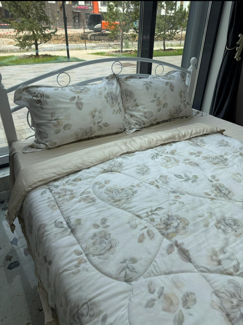 A bed with white metal frame and floral patterned bedding is positioned in front of a window.