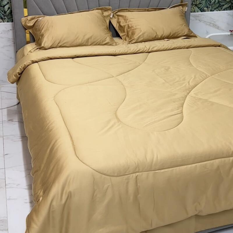 A bed with a gray headboard is covered with a gold comforter and two matching pillows.