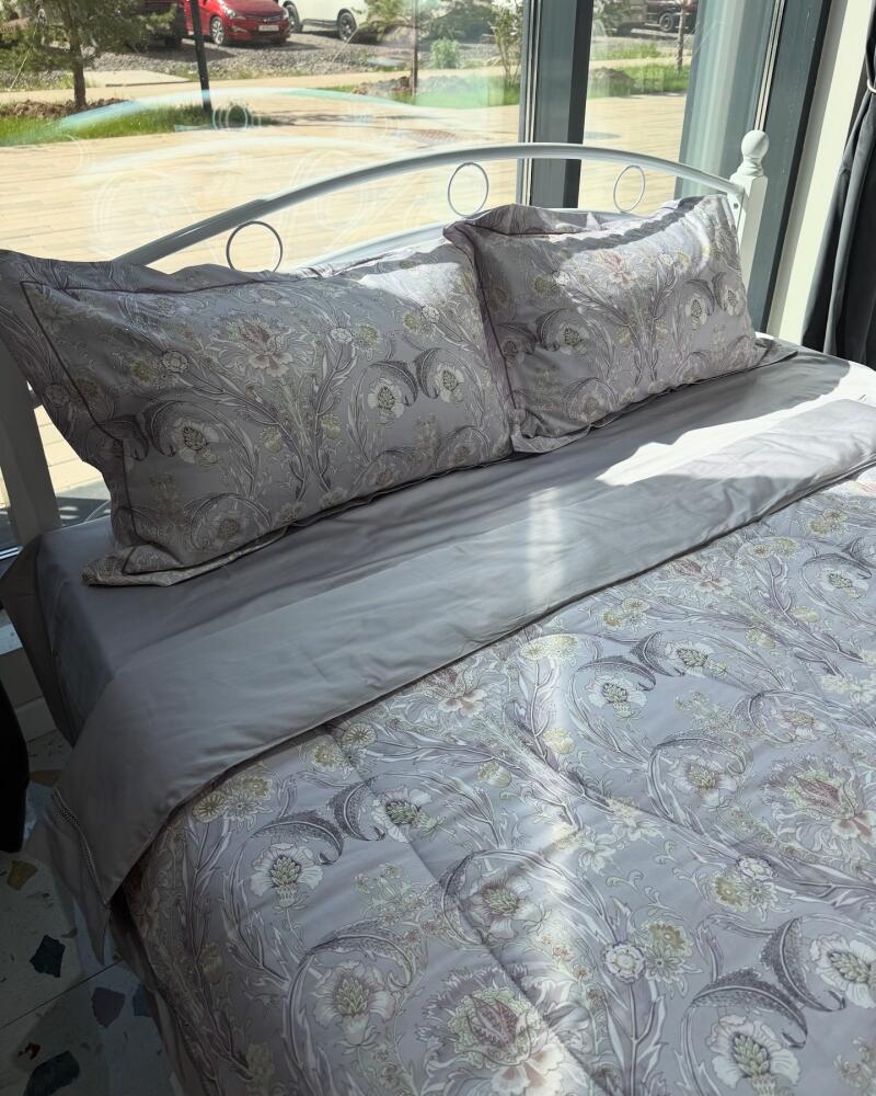 A bed with a white metal frame is neatly made with floral-patterned bedding and pillows in shades of grey and white.