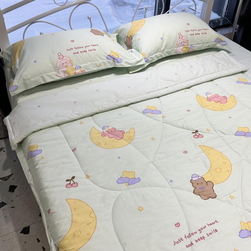 A bed is covered with a light green comforter and matching pillows, featuring cartoon designs of crescent moons, sleeping bears, clouds, stars, and cherries, along with the text 'Just follow your heart and keep smile'.