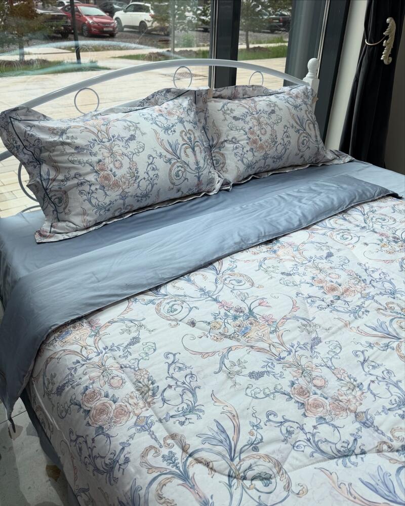 A bed with a white metal frame is neatly made with floral patterned bedding and solid gray sheets and pillowcases.